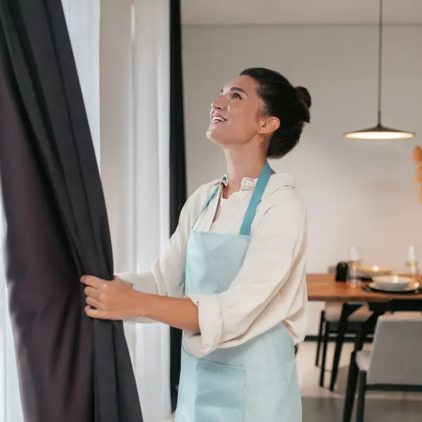 young woman standing near widnow fixing curtains
